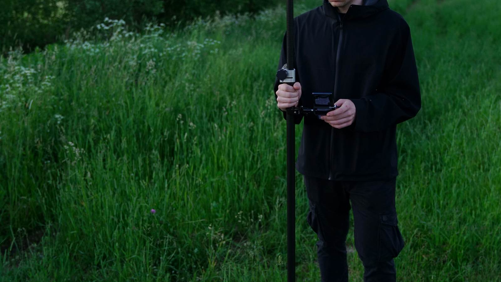 Surveyor holding a pole-mounted controller in a grassy field