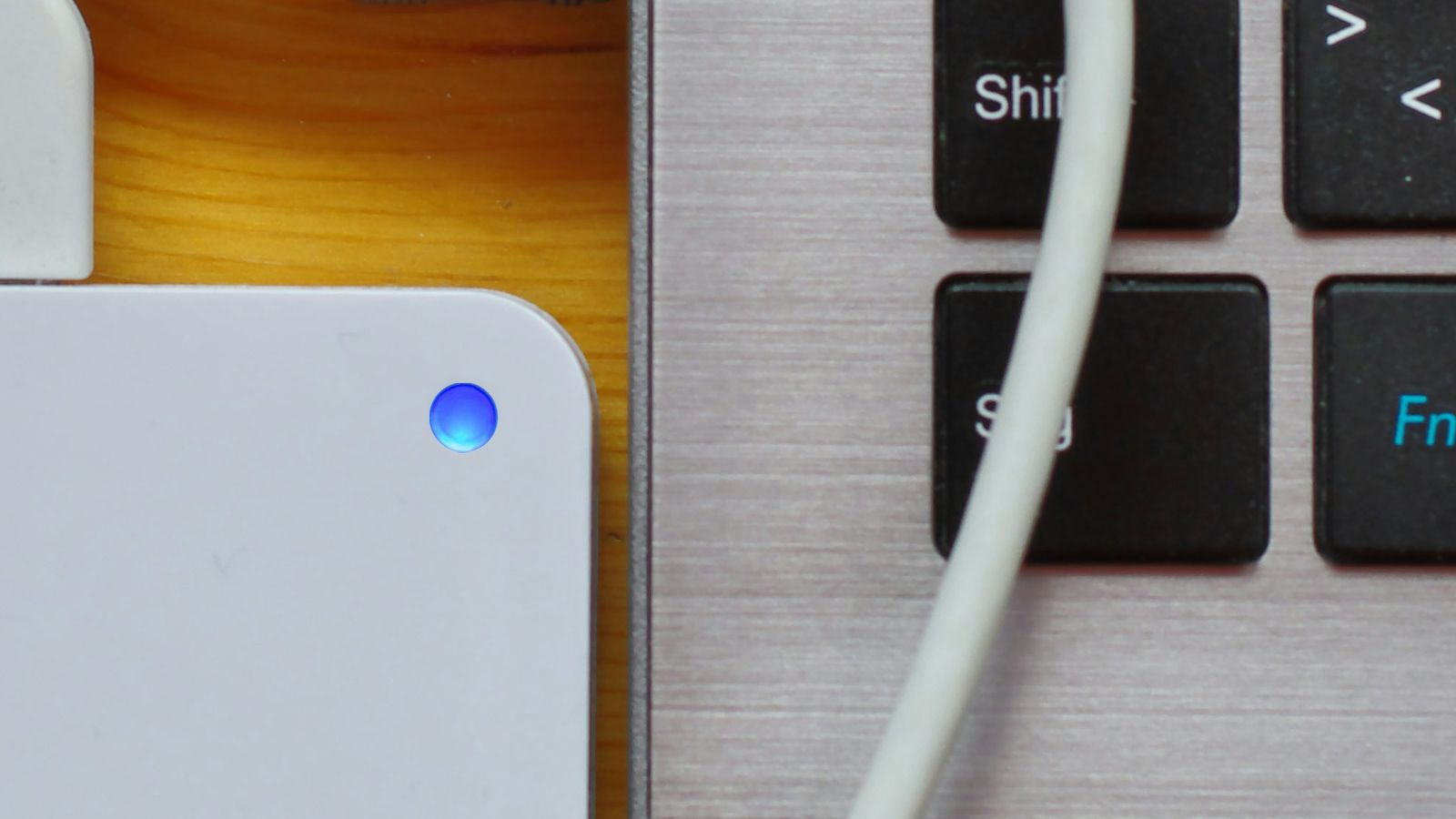White external drive with a blue status light beside a laptop and cable