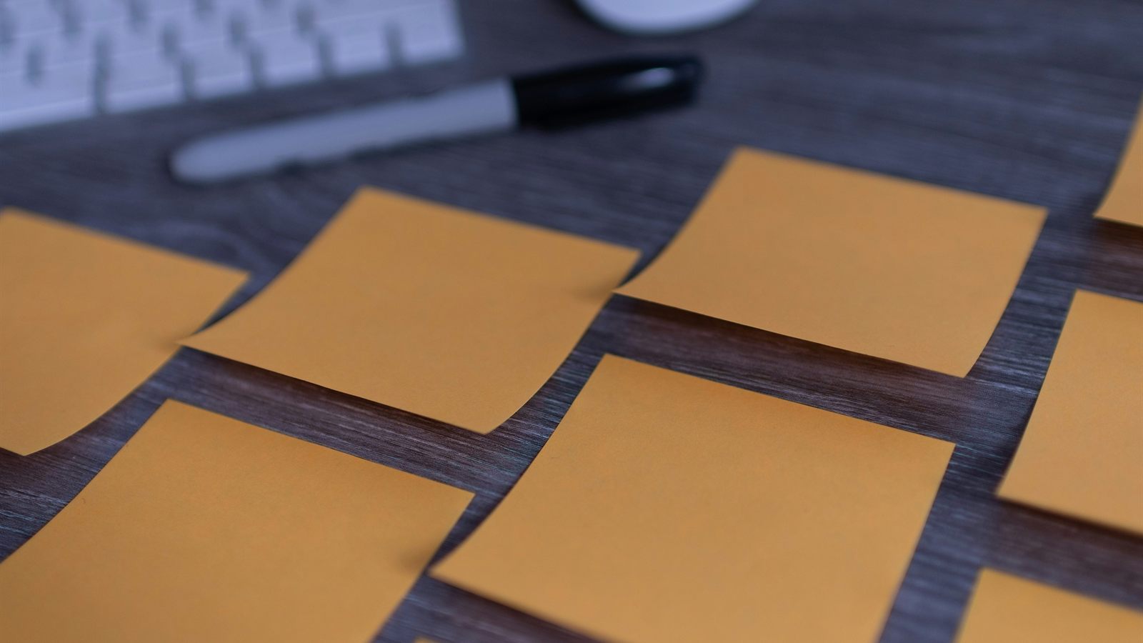 Blank sticky notes arranged beside a marker on a dark tabletop.